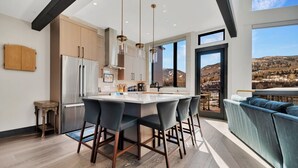 A modern kitchen with a central island, stainless steel appliances, and a view of a mountainous landscape through large windows.