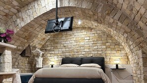 Una camera da letto con soffitto a volta in pietra, un letto con testiera nera e una TV a parete.