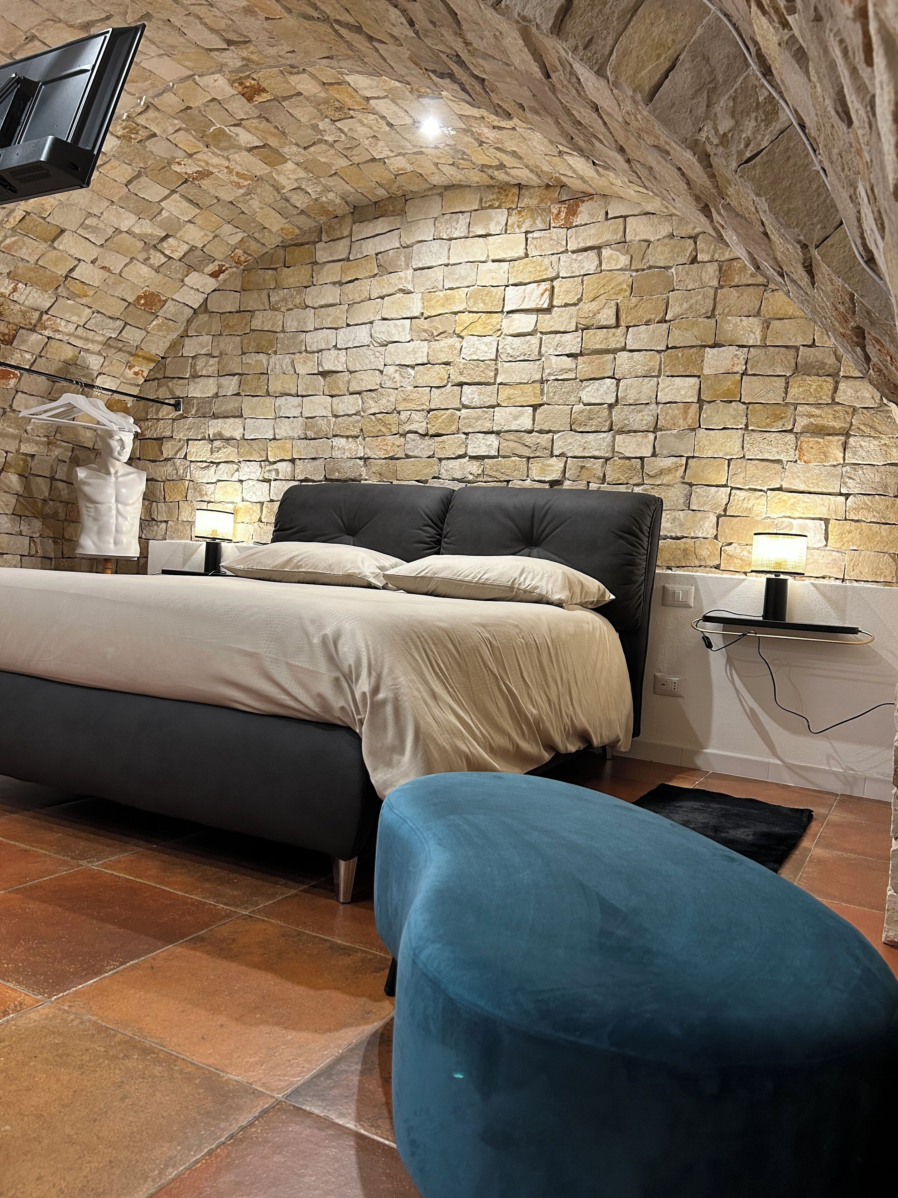 Ein Schlafzimmer mit Stehwand, einem Bett, einem blauen Sessel und einem an der Wand befestigten Flachbildfernseher.