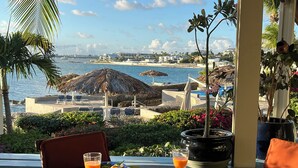 Un tavolo apparecchiato con piatti, bicchieri e una pianta in vaso, con vista sulla spiaggia e sull'oceano.