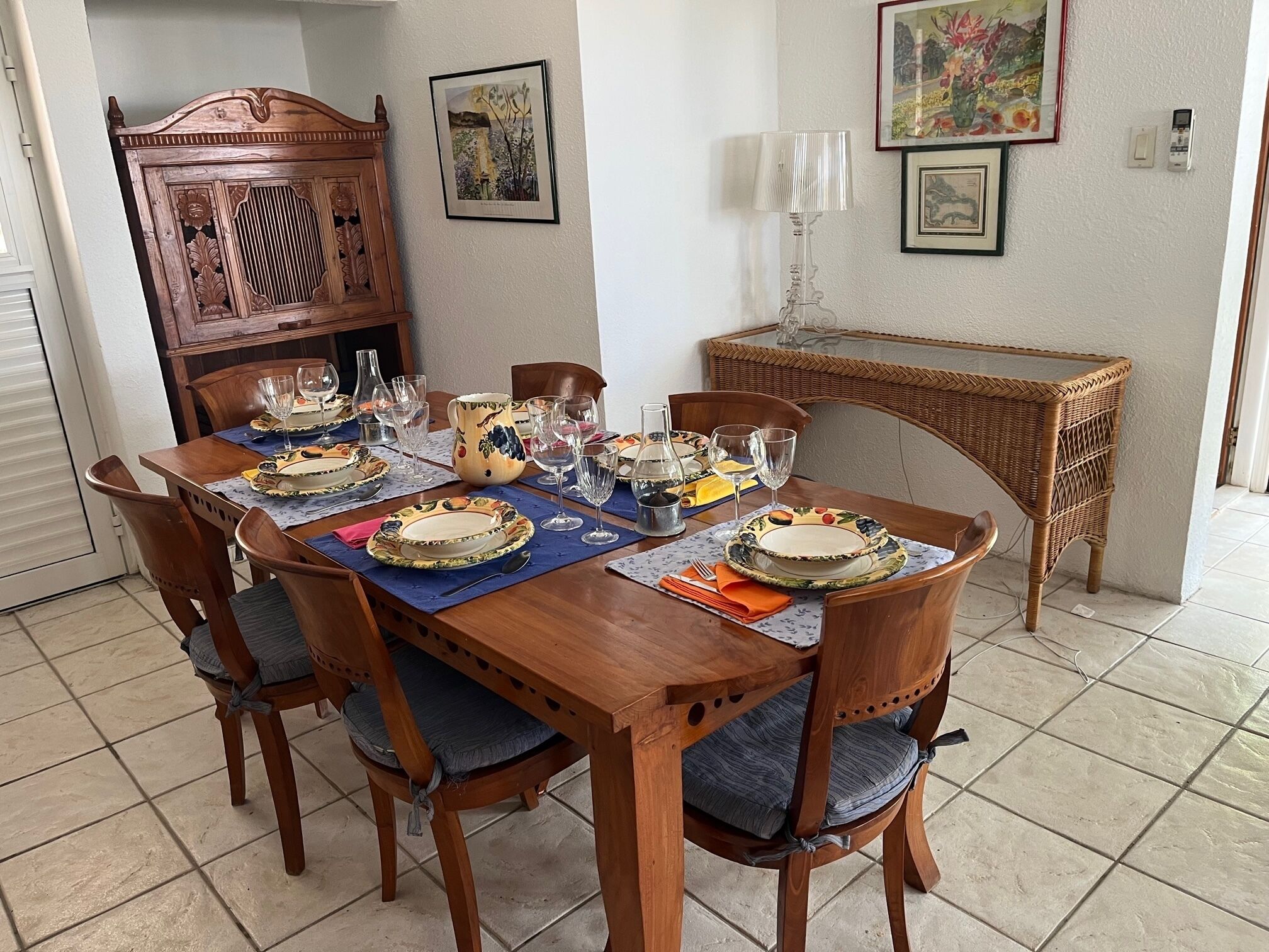 A dining area with a wooden table set for a meal, surrounded by chairs with blue cushions.