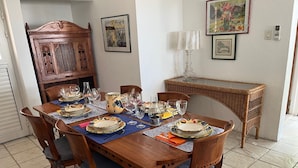 Zona pranzo con tavolo in legno apparecchiata per un pasto, circondata da sedie con cuscini blu.