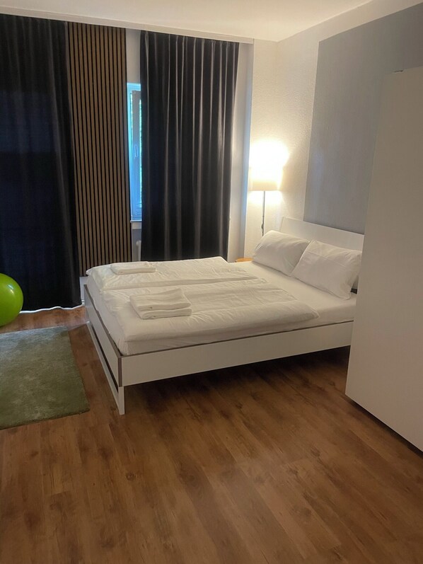 A neatly made bed with white linens, a green exercise ball, and a wooden floor.