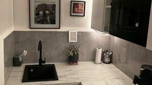 A modern kitchen with a black sink, white cabinets, a marble countertop, a microwave, and framed pictures on the wall. - Quiet apartment 4 min from the cathedral with office and balcony (Köln)