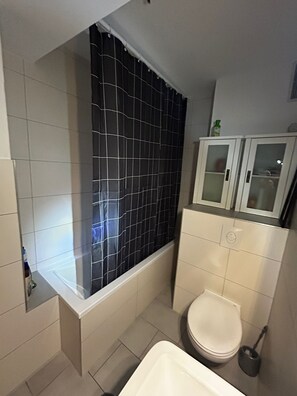 A bathroom with a bathtub, toilet, and a cabinet.