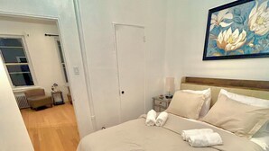 Une chambre à coucher avec un grand lit, une table de chevet, une chaise et une porte donnant sur une autre pièce.