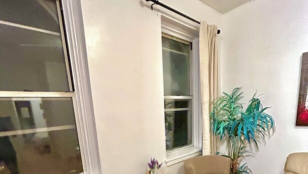 Un salon avec deux fauteuils beiges, une petite table d’appoint noire ornée d’un vase et de bougies, et une plante en pot.