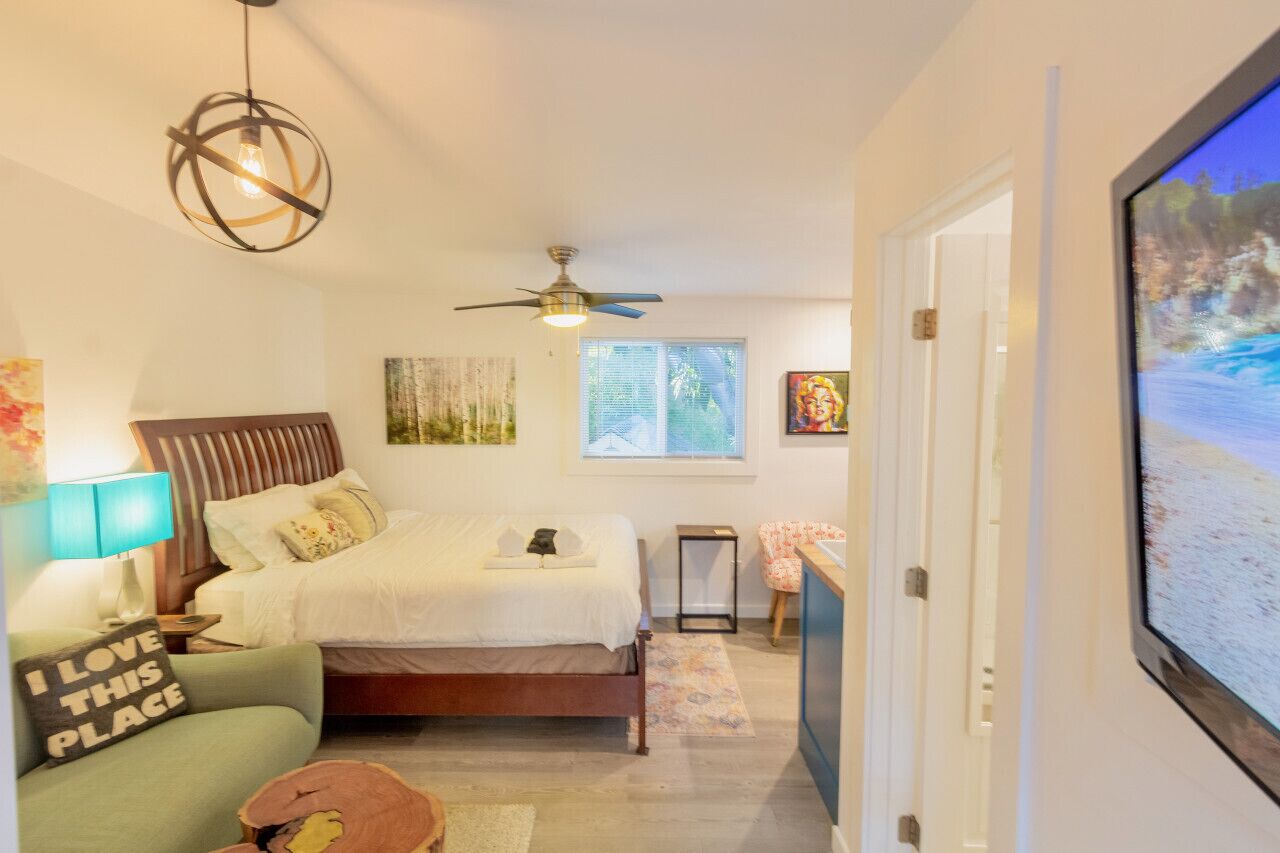 Ein Schlafzimmer mit einem Bett, einem Deckenventilator, einem Fernseher und Kunstwerken an den Wänden.