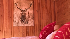 A wooden cabin room with a framed deer picture on the wall, a bed with red pillows, and a lamp on the bedside table. - Chalet Glemm Alpin (Hinterglemm)