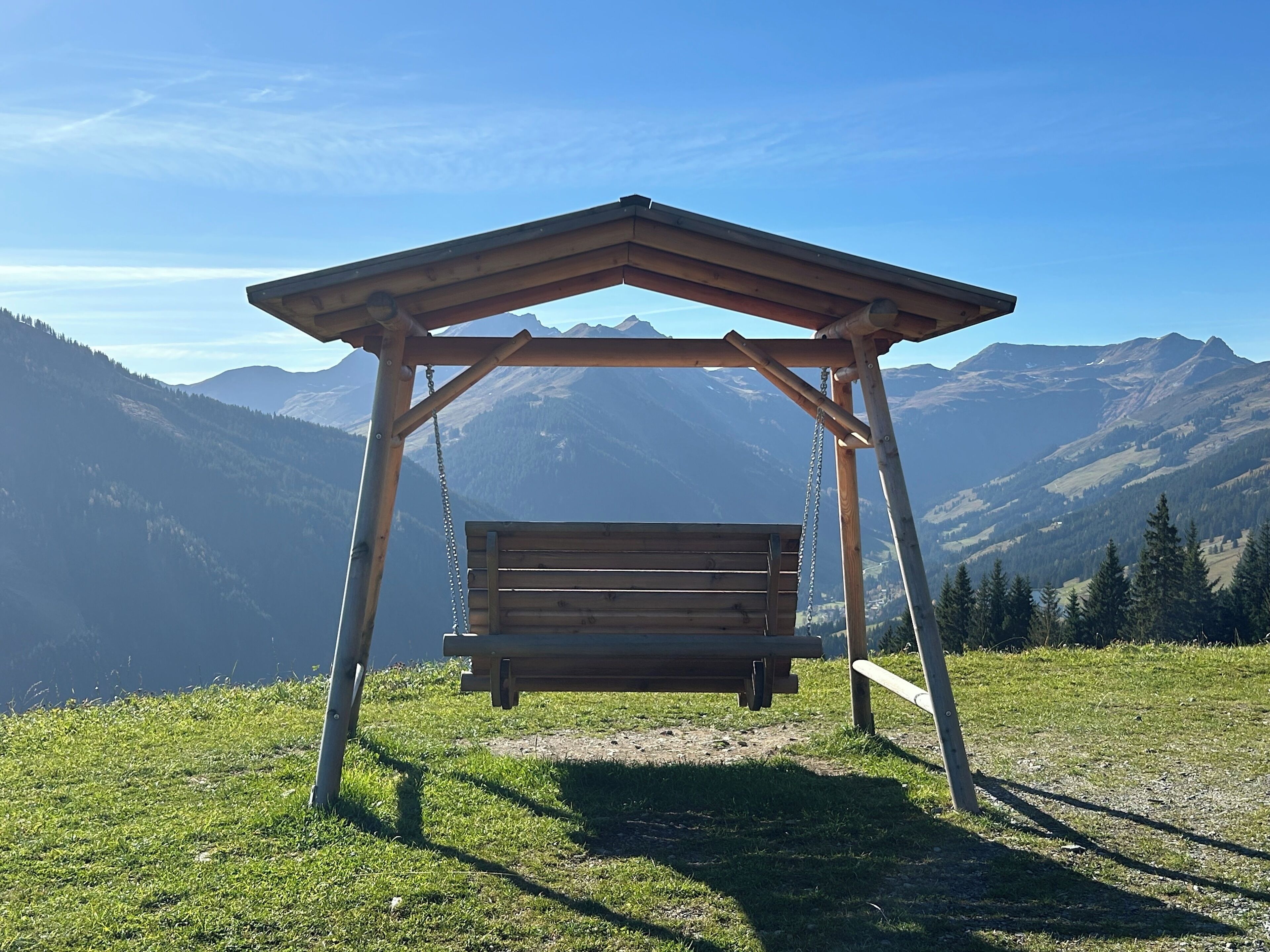 Een houten schommelbank onder een pergola, met uitzicht op een berg.