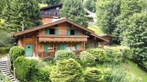 A wooden chalet with a balcony, surrounded by lush greenery and a mountain backdrop. - Chalet Glemm Alpin (Hinterglemm)