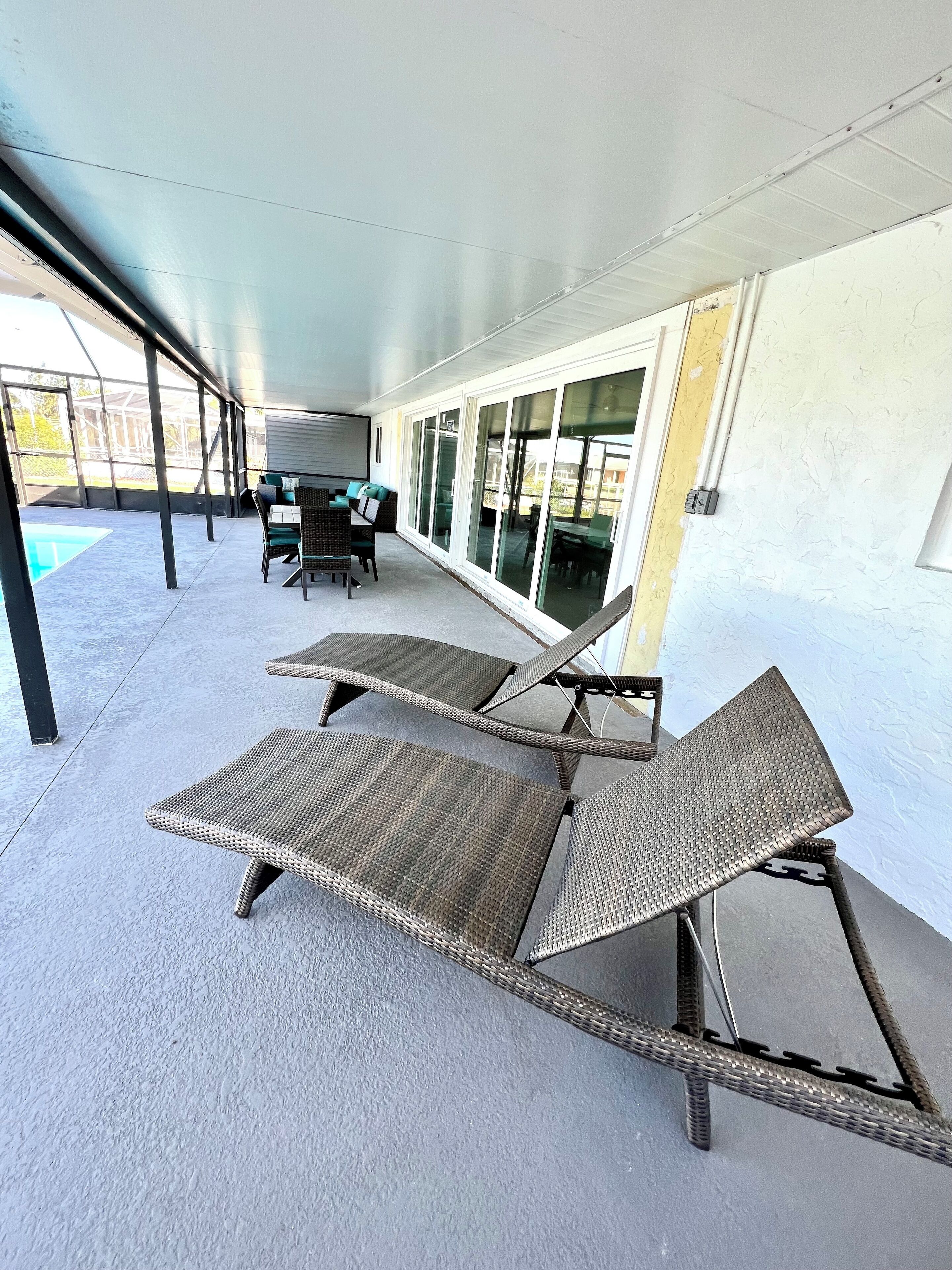Ein überdachter Patio-Bereich mit Korlounge-Stühlen, einem Tisch und einem Pool.