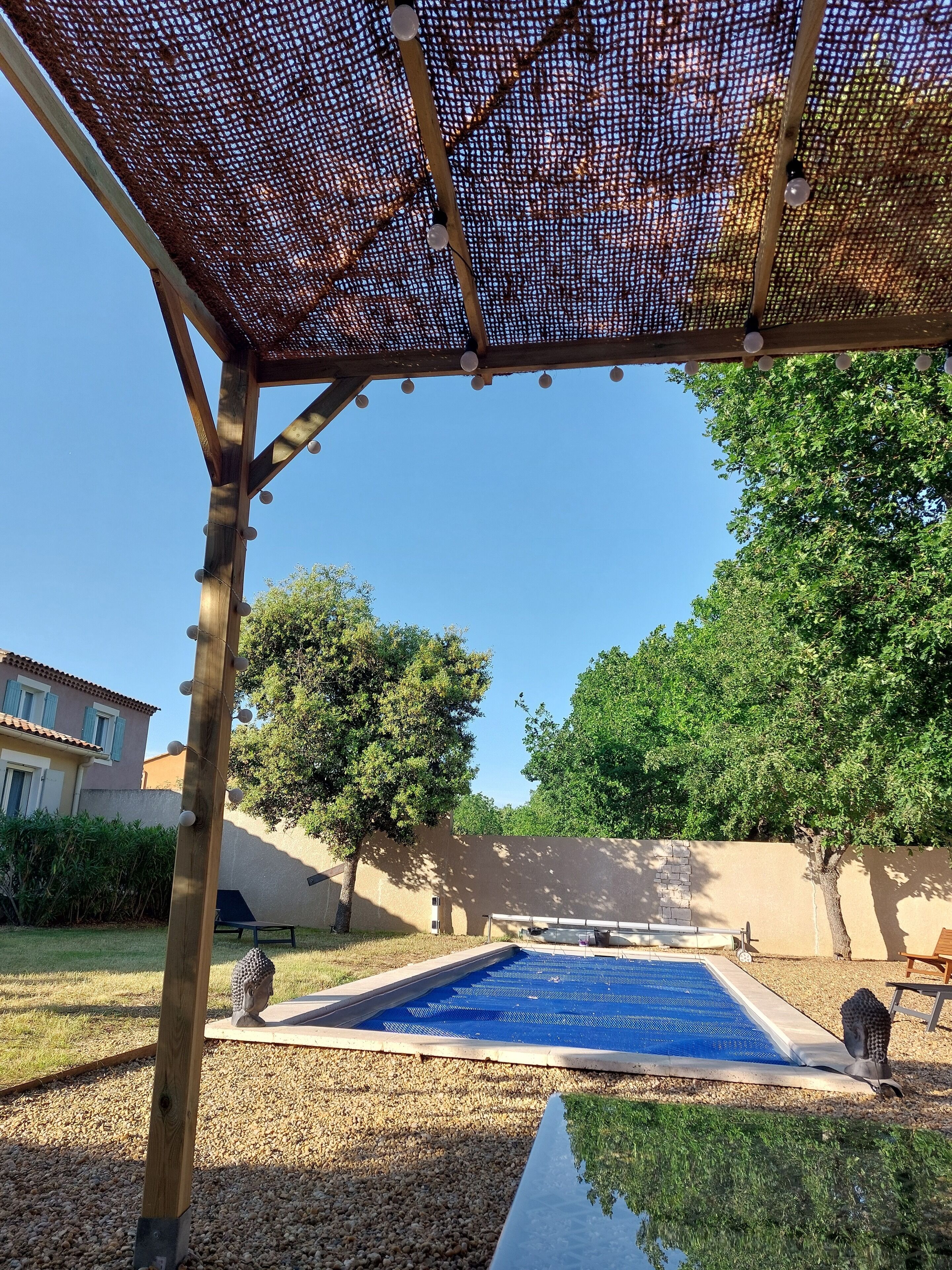 Ett takförsett utomhusområde med en pool, en träpergola och en staty.