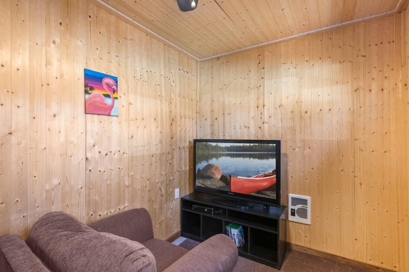 Et værelse med træpaneler, et fjernsyn, en sofa og et billede på væggen.