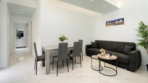 Un soggiorno moderno con zona pranzo, un divano grigio scuro, un piccolo tavolo rotondo e un quadro appeso al muro.