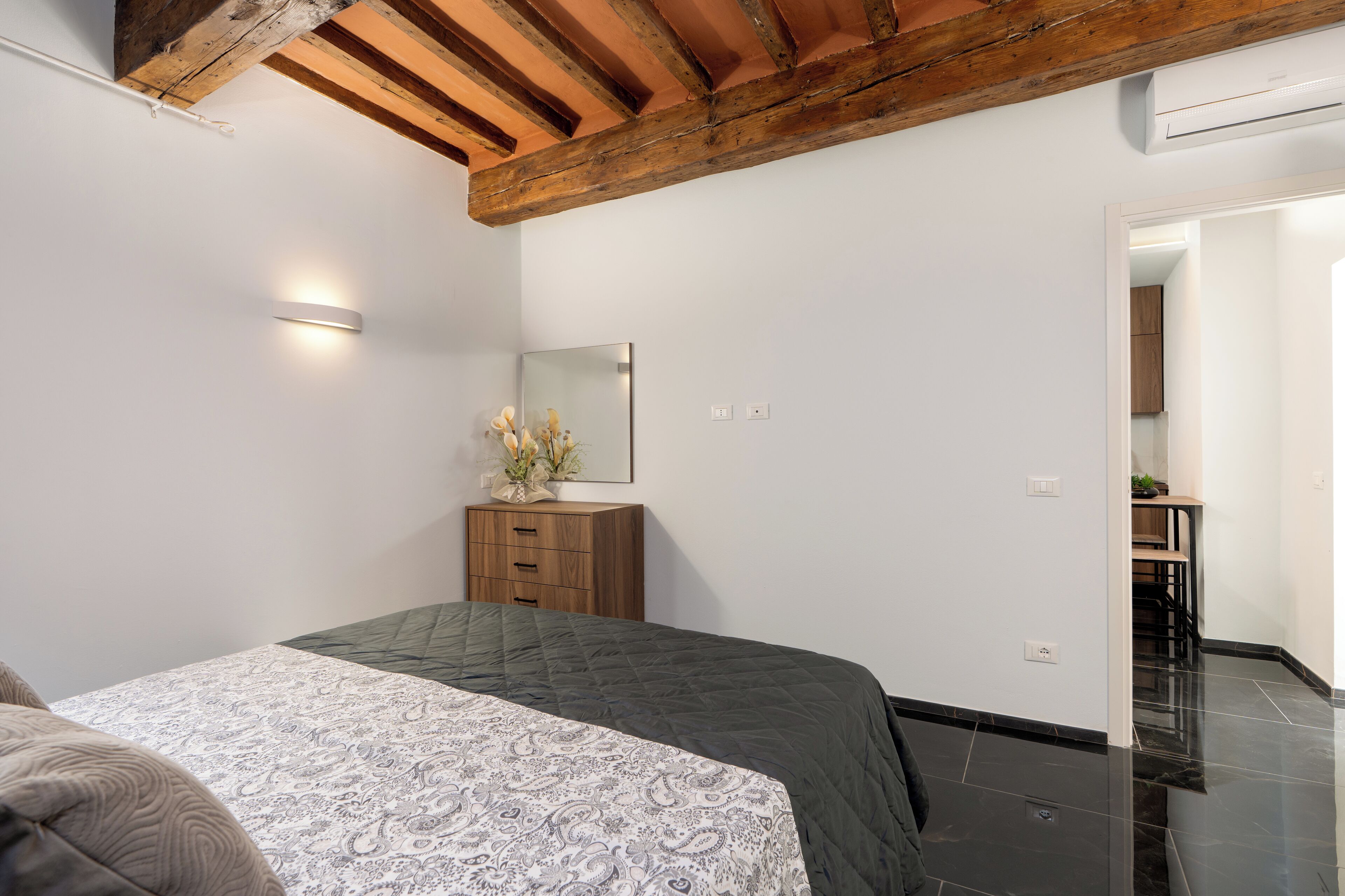 A bedroom with a bed, a wooden dresser, a mirror, and a door leading to a bathroom.