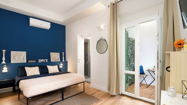 Una camera da letto con un letto, un comodino, uno specchio e una porta vetrata scorrevole che dà su uno spazio all'aperto.