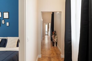 Ein Flur mit Holzboden, einem Bett mit blauer und weißer Bettdecke und einer Wand mit gerahmten Bildern.