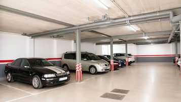 Un parking à plusieurs niveaux où plusieurs voitures sont garées sous un plafond en béton, avec des tuyaux apparents.