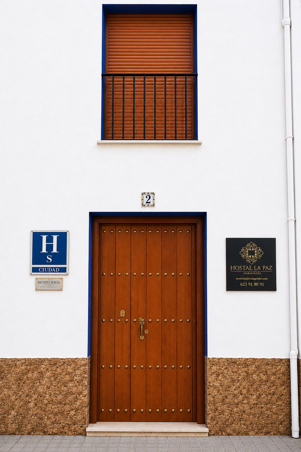 Een hotelentree met een houten dubbele deur, met het cijfer '2' erboven, en borden waarop 'HOSPEDERÍA' en 'HOSTAL LA PAZ' staan.