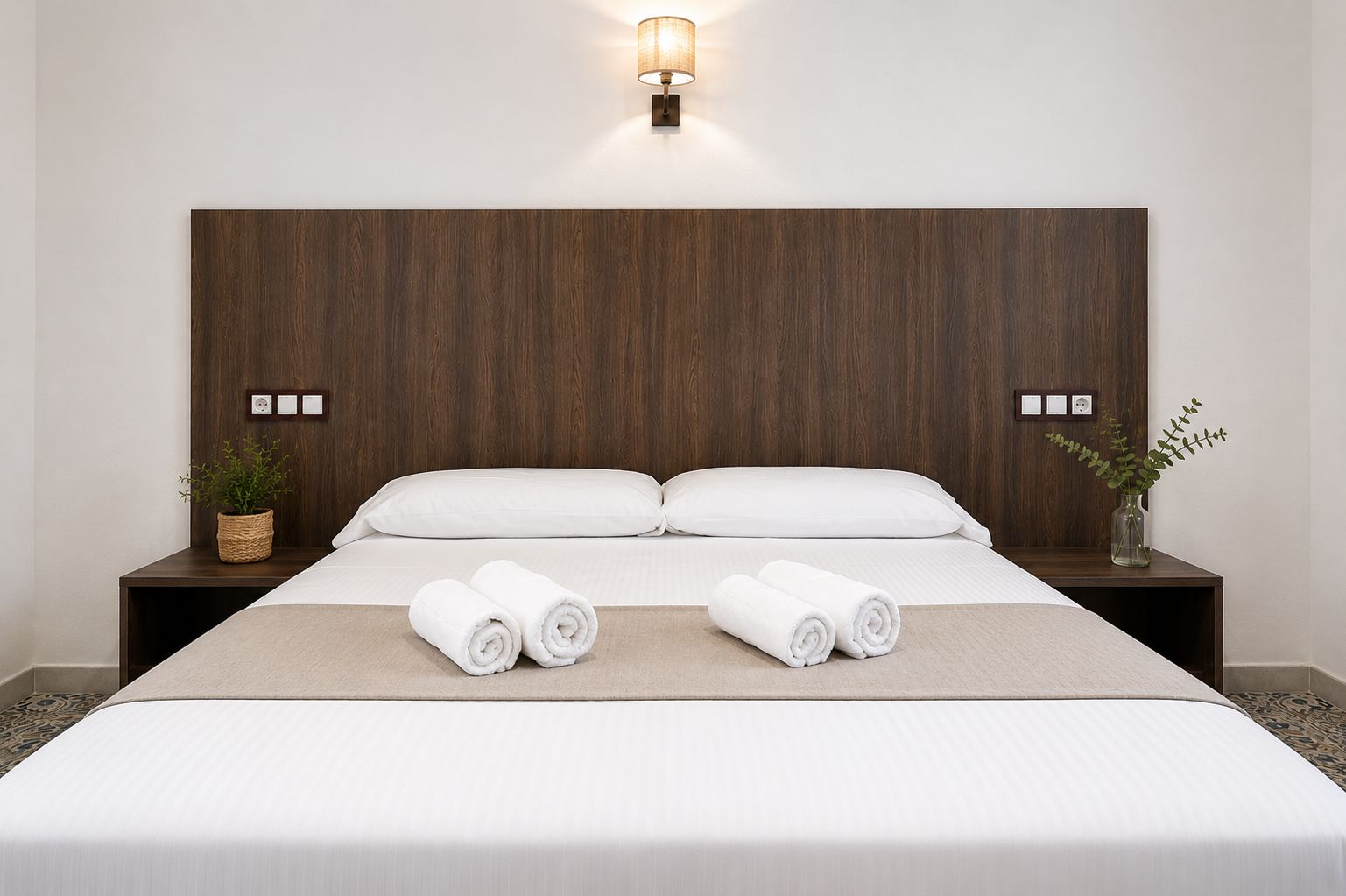 Ein Hotelzimmer mit einem großen Bett, zwei Nachttischen, einer Wandleuchte und einem Blumentopf.