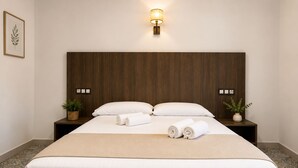 Une chambre d’hôtel avec un grand lit, deux tables de chevet, une lampe fixée au mur et une plante décorative accrochée au mur.