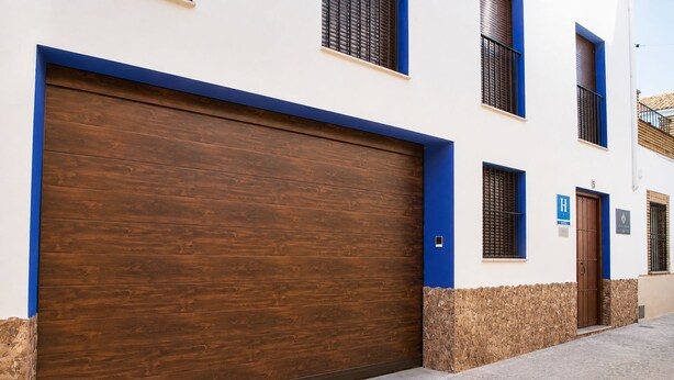 Un bâtiment doté d’une grande porte de garage en bois, d’un socle en pierre et de bordures bleues.