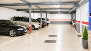 Un parking à plusieurs niveaux où les voitures sont garées en rangées, avec des grilles de ventilation dans le sol et une plante en pot près du mur.