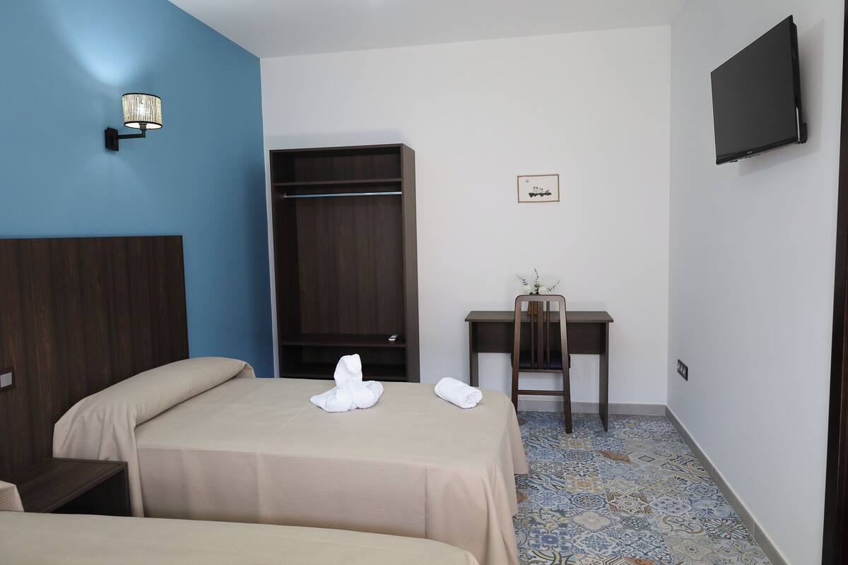 Habitación de hotel con dos camas, un escritorio, una silla, un armario, un televisor y un piso con diseño.