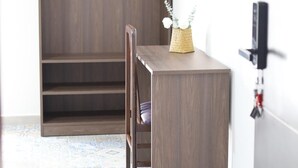 Een kamer met een houten bureau, een stoel, een aan de muur bevestigde televisie en een kledingkast.