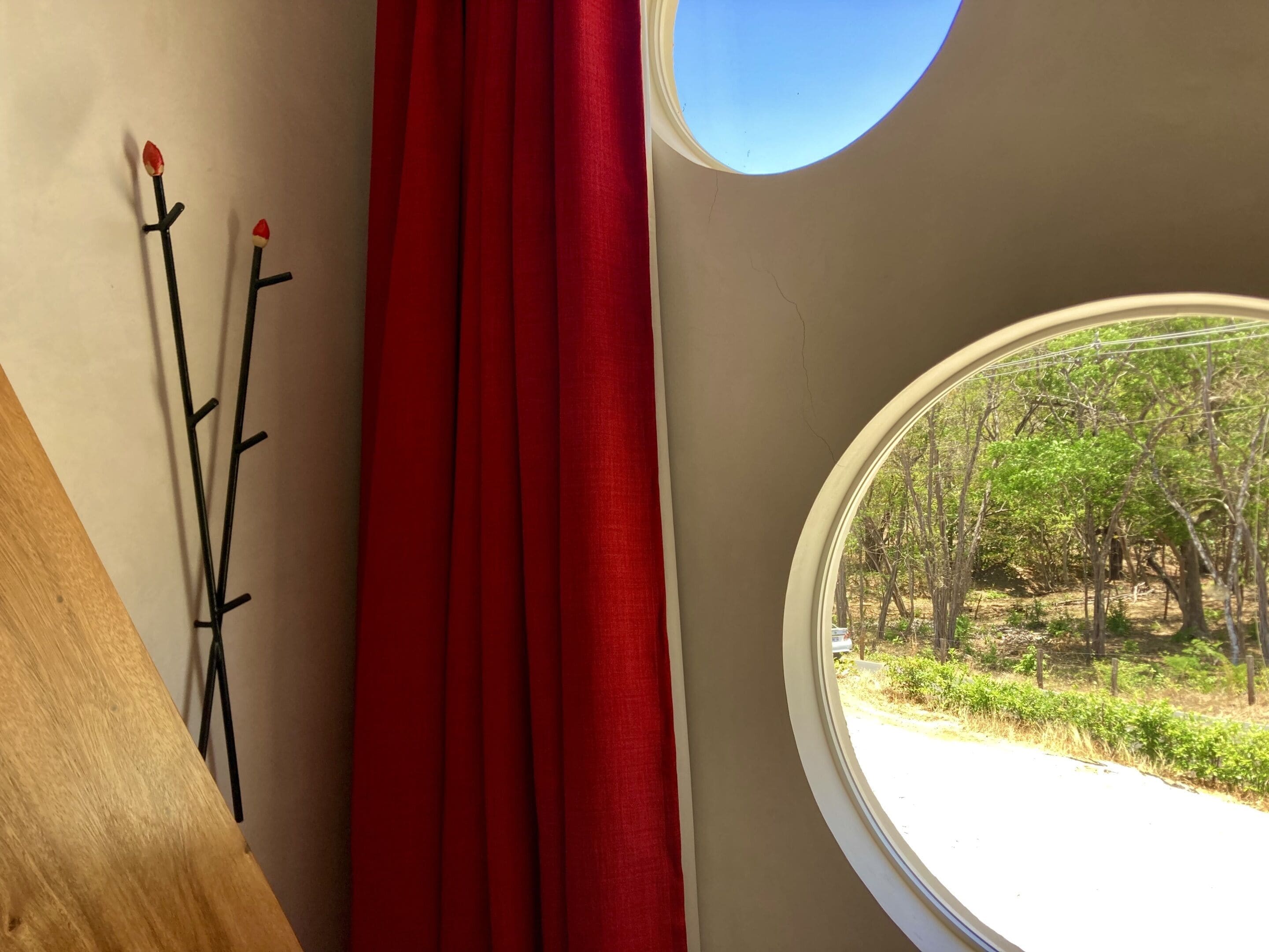 A room with a wooden floor, a red curtain, and a window with a view of trees and greenery outside.