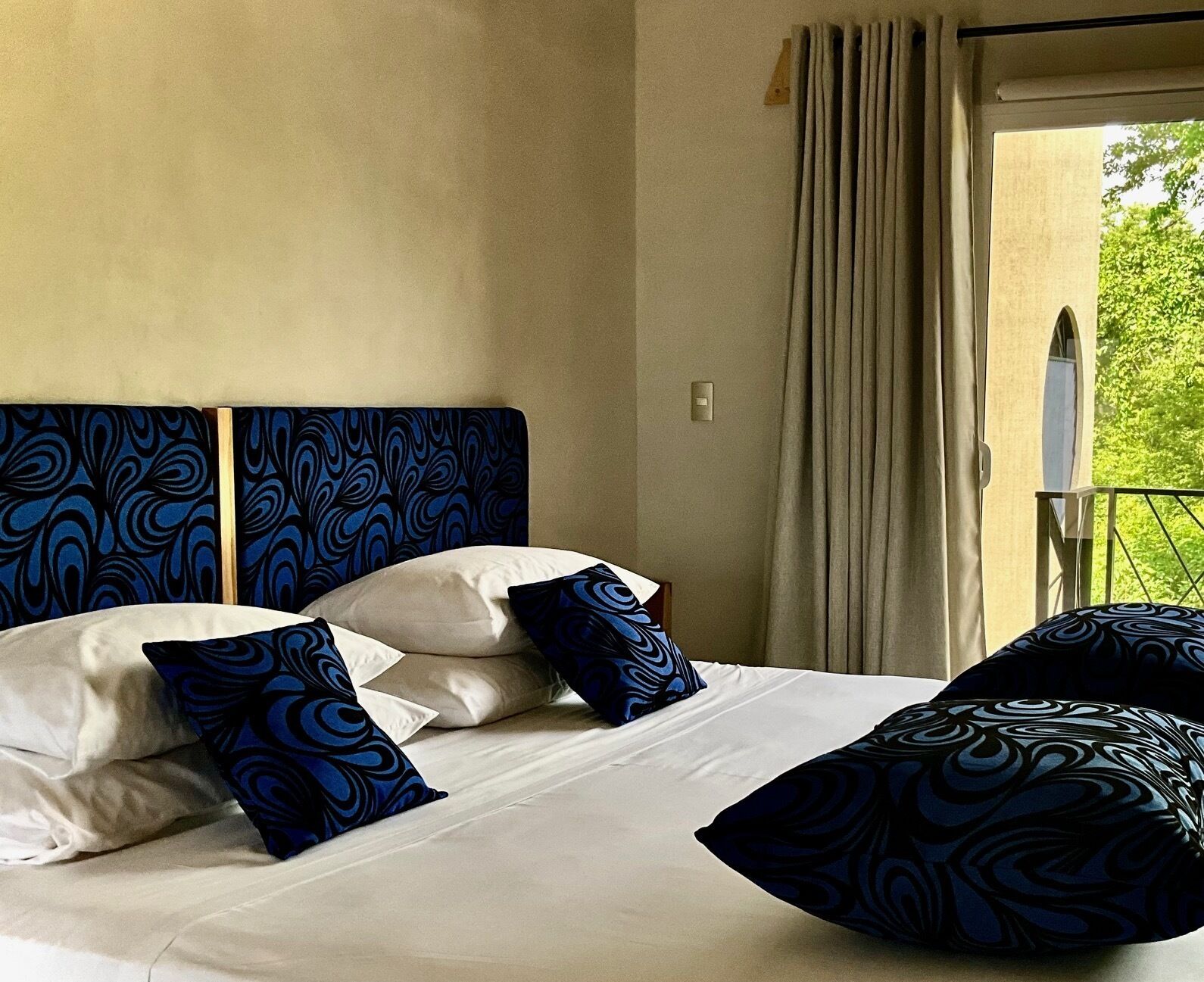 Habitación de hotel con cama, cabecero estampado en azul y vistas a zonas verdes.