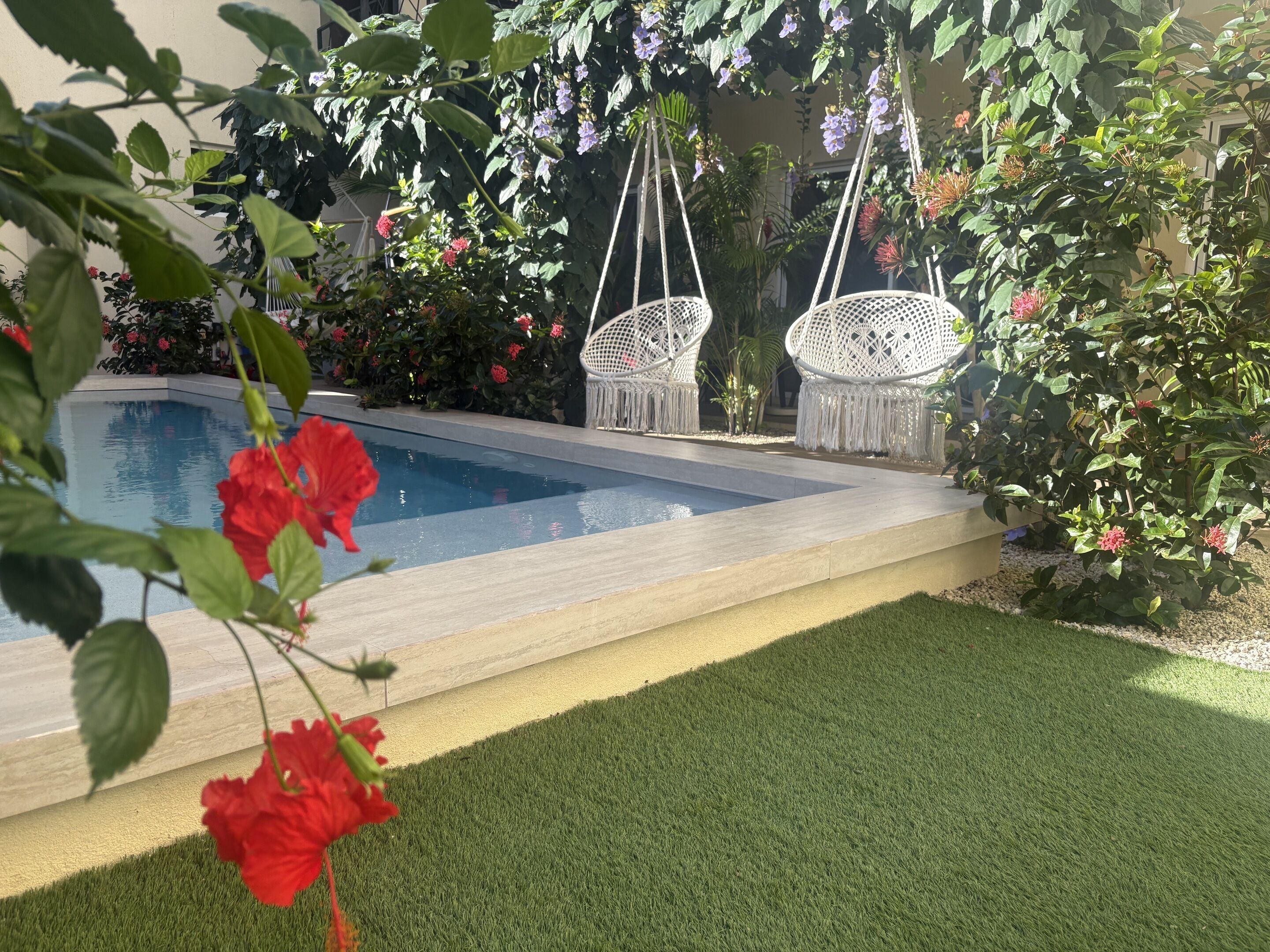 A swimming pool with a grassy area and hanging chairs.