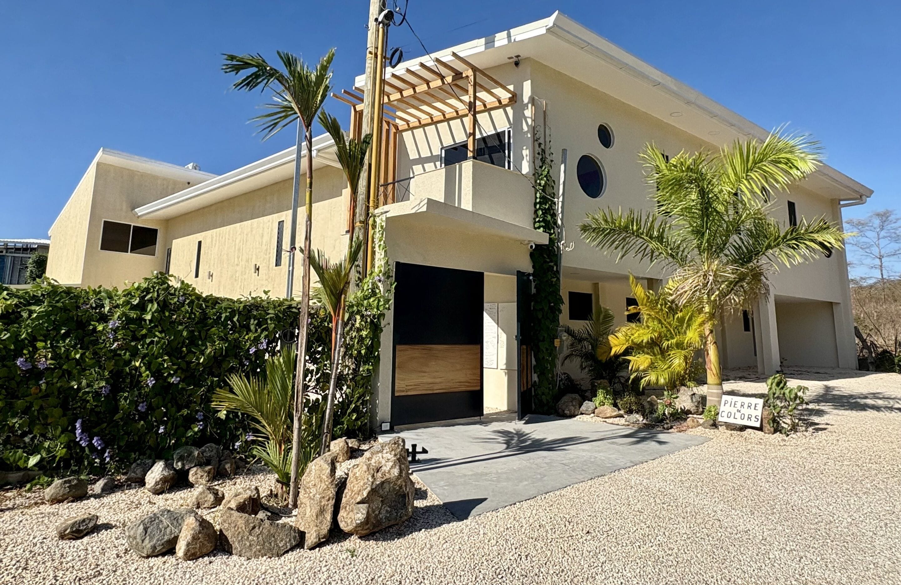 A modern two-story house with a covered patio, a garage, and a well-maintained garden with rocks and plants.