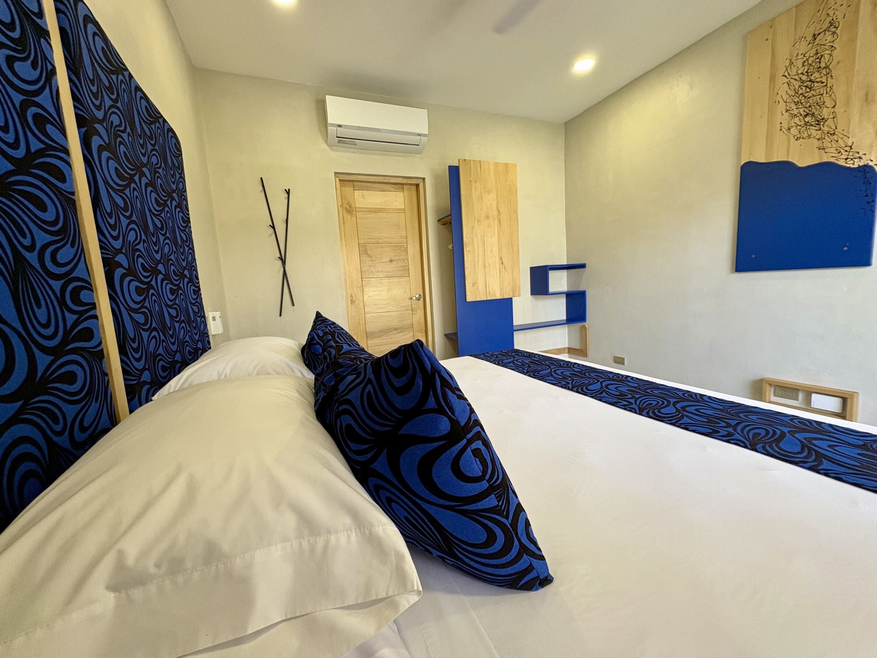 Ein Schlafzimmer mit einem Bett, einer Holztür, einer Klimaanlage und einer blauen Wanddekoration.