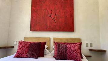 Une chambre d’hôtel avec un grand tableau abstrait rouge au mur, deux têtes de lit en bois et des coussins assortis à motifs.