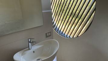 Une salle de bain avec un lavabo blanc, un miroir et une fenêtre ornée d’une grille métallique.