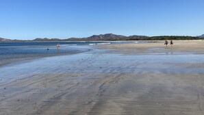 Una spiaggia con cieli sereni, acque calme e montagne sullo sfondo.