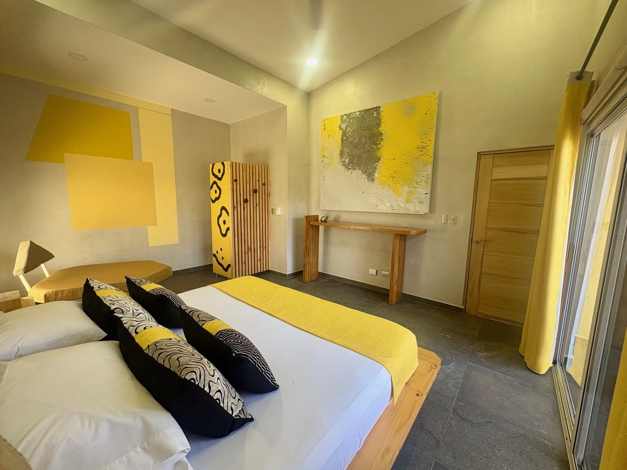 Un dormitorio moderno con una cama grande, un banco de madera, un armario y un cuadro en la pared.