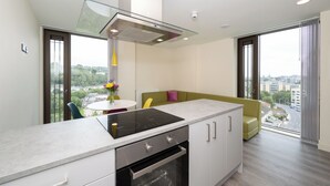 A modern kitchen with a built-in stove, oven, and a glass hood. There is a dining area with a table and chairs, and a view of the city through large windows. - Crow's Nest (Cork)