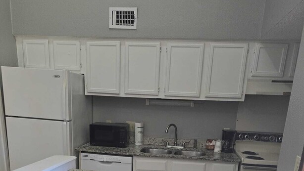 A compact kitchen with white cabinets, a microwave, a stove, and two wooden chairs with intricate designs. - Furnished and Spacious 2-Bedroom Apartment in Downtown Dallas Medical District (Dallas)