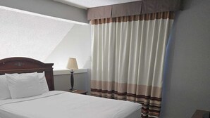 A hotel room with a large bed, a bedside table, a lamp, and a window with curtains. - Furnished and Spacious 2-Bedroom Apartment in Downtown Dallas Medical District (Dallas)