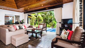 A spacious living room with a wooden ceiling, a large TV, and a pool view. - Beachfront Villa in  Playa Langosta, Tamarindo! (Playa Langosta)