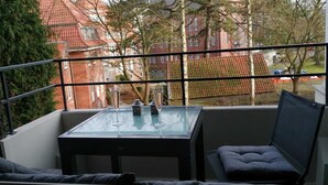 A balcony with a glass table, two chairs, and a view of red-roofed buildings.