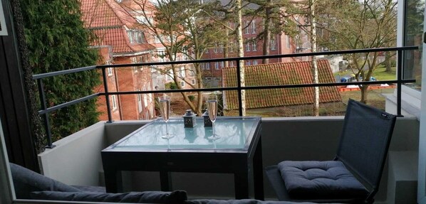 A balcony with a glass table, two chairs, and a view of red-roofed buildings. - Carpe Diem - Beachfront Apartment with Pool (Timmendorfer Strand)