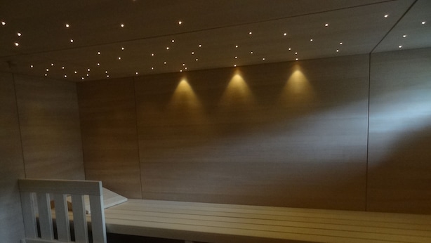 A sauna with a bench, wooden walls, and ceiling lights.