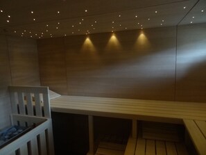 A sauna with a bench, wooden walls, and ceiling lights. - Carpe Diem - Beachfront Apartment with Pool (Timmendorfer Strand)