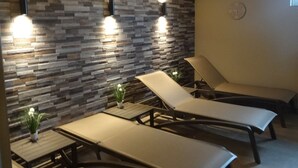 A spa area with two lounge chairs, a stone wall, and a clock on the wall.