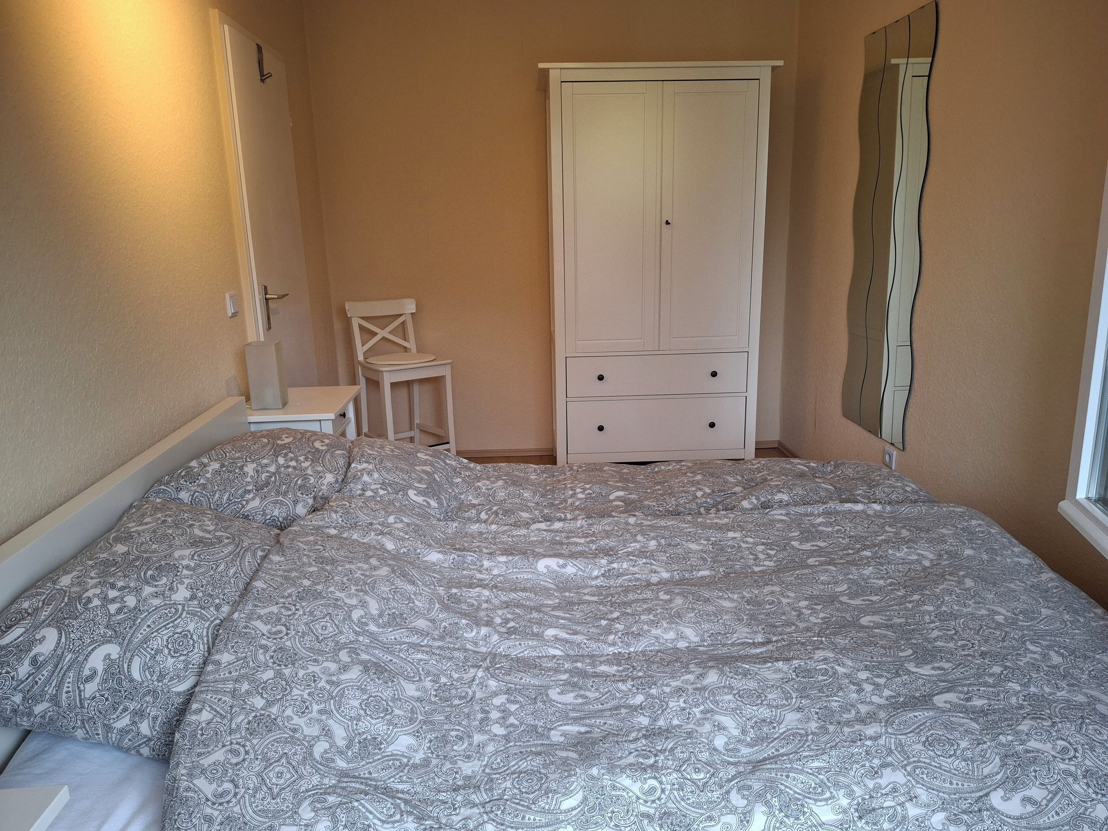 Ein Schlafzimmer mit Bett, Stuhl, Kleiderschrank und Spiegel.