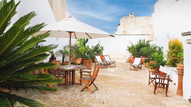 An outdoor patio with stone flooring, wooden furniture, and potted plants. - Palazzo Insula (Gallipoli)